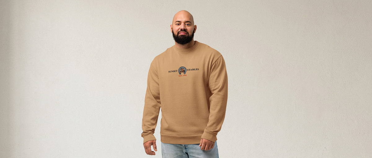 Fashionable male model wearing a burro brown tri-blend fleece sweatshirt featuring a fan-made sunset stables ranch design embroidered across the front and setshirt number 6405 on the sleeve. Item is a BRKDrip Limited Edition Cozy Wear Sweatshirt.