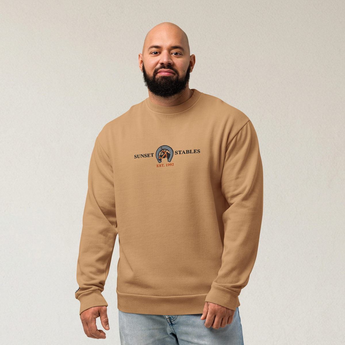 Fashionable male model wearing a burro brown tri-blend fleece sweatshirt featuring a classic fan-made sunset stables ranch design embroidered across the front and setshirt number 6405 on the sleeve. Item is a BRKDrip Limited Edition Cozy Wear Sweatshirt with a classic town building blocks aesthetic.